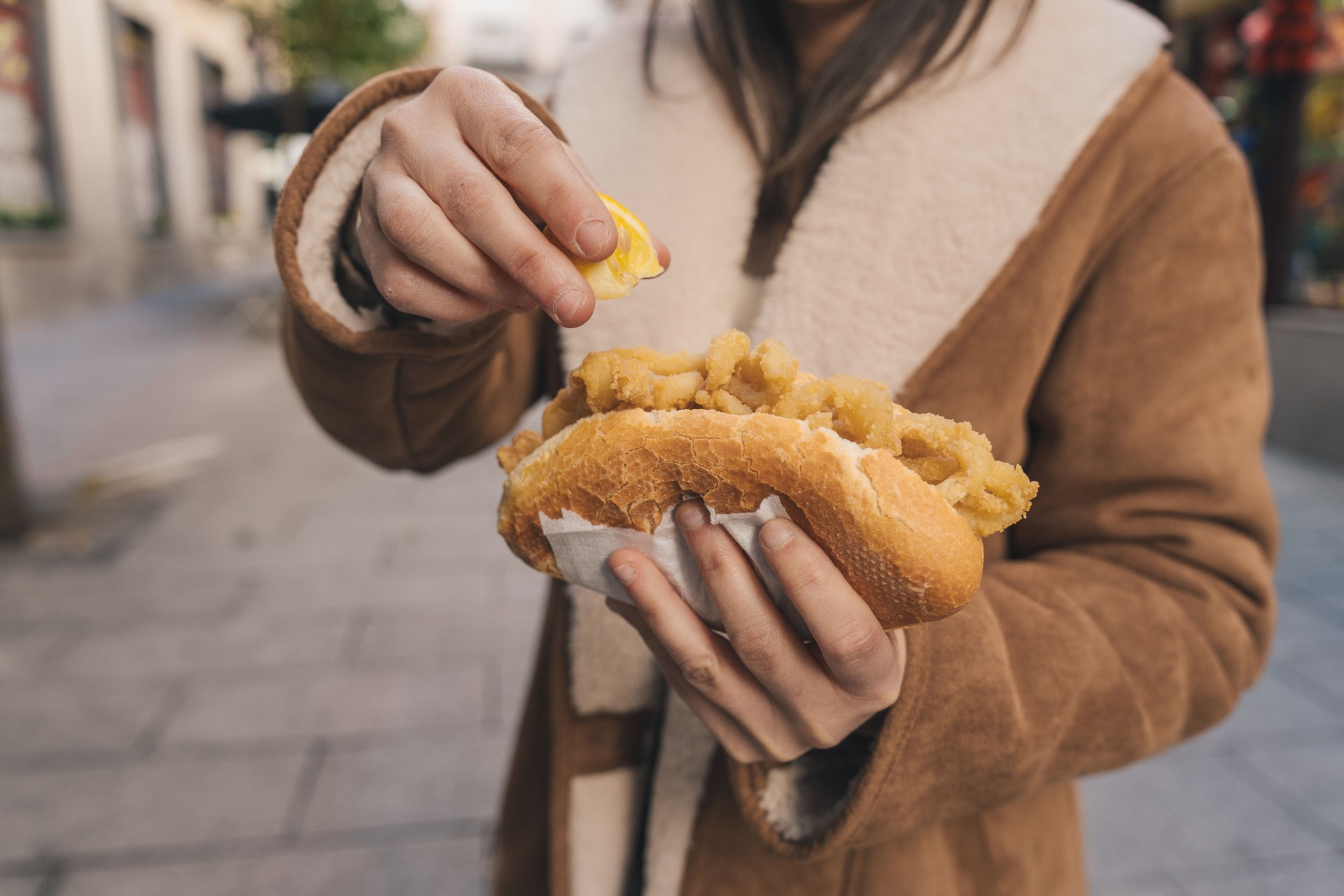Woman squeezing lemon on fried calamari sandwich in the street